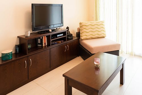 ein Sideboard auf dem ein Flachbild-Smart-TV steht. Daneben ein Sessel und im Vordergrund ein kleiner Wohnzimmertisch